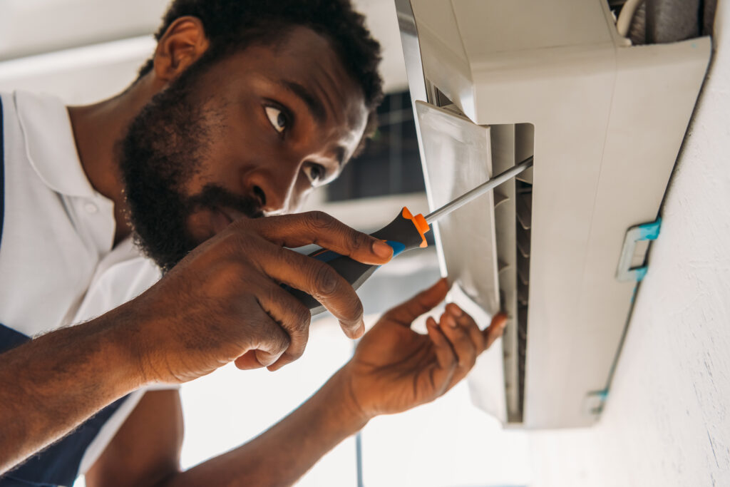Air conditioner replacement: Technician repairs AC unit with screwdriver. Consider AC replacement tips for efficiency | Accurate Air