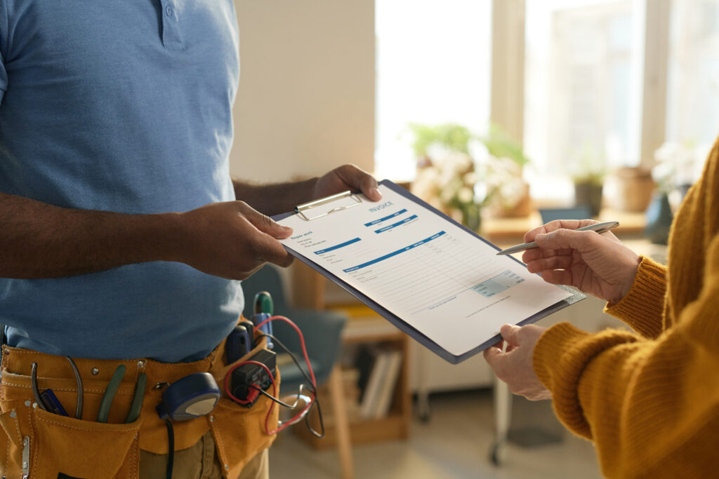 HVAC technician in a toolbelt handing a clipboard with service details to a client, emphasizing home comfort and maintenance discussions.