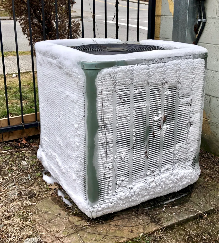 Ice-covered AC unit with frost accumulation on coils, illustrating potential HVAC issues during summer heat.