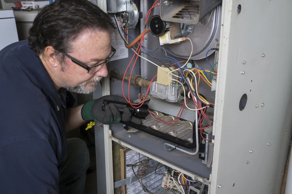 HVAC technician inspecting furnace components and wiring for maintenance and troubleshooting issues.