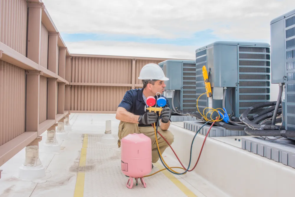 HVAC technician using refrigerant gauges and equipment on rooftop air conditioning units, highlighting important HVAC refrigerant changes in 2024.