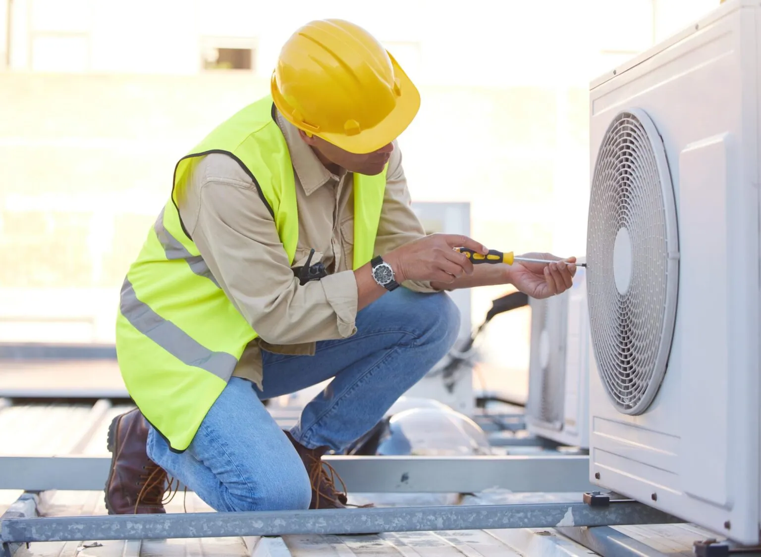 A technician in a hard hat and safety vest working on a heat pump unit on a rooftop.