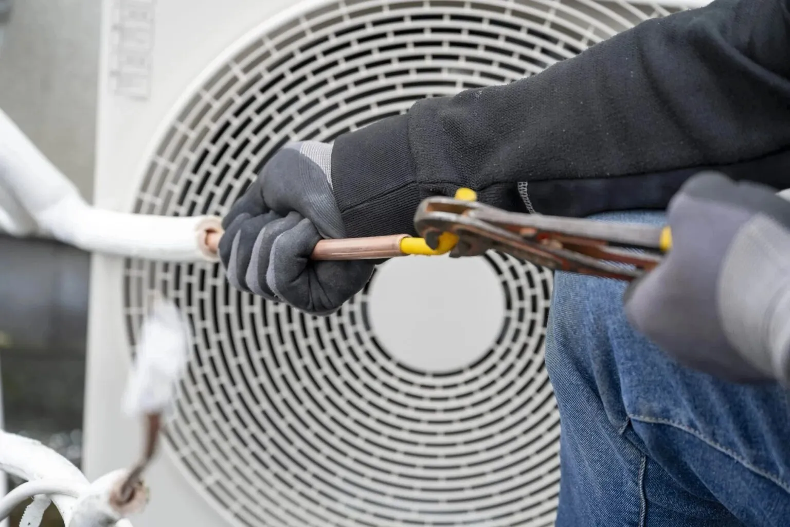 A gloved technician working on the copper line set of an outdoor heat pump.
