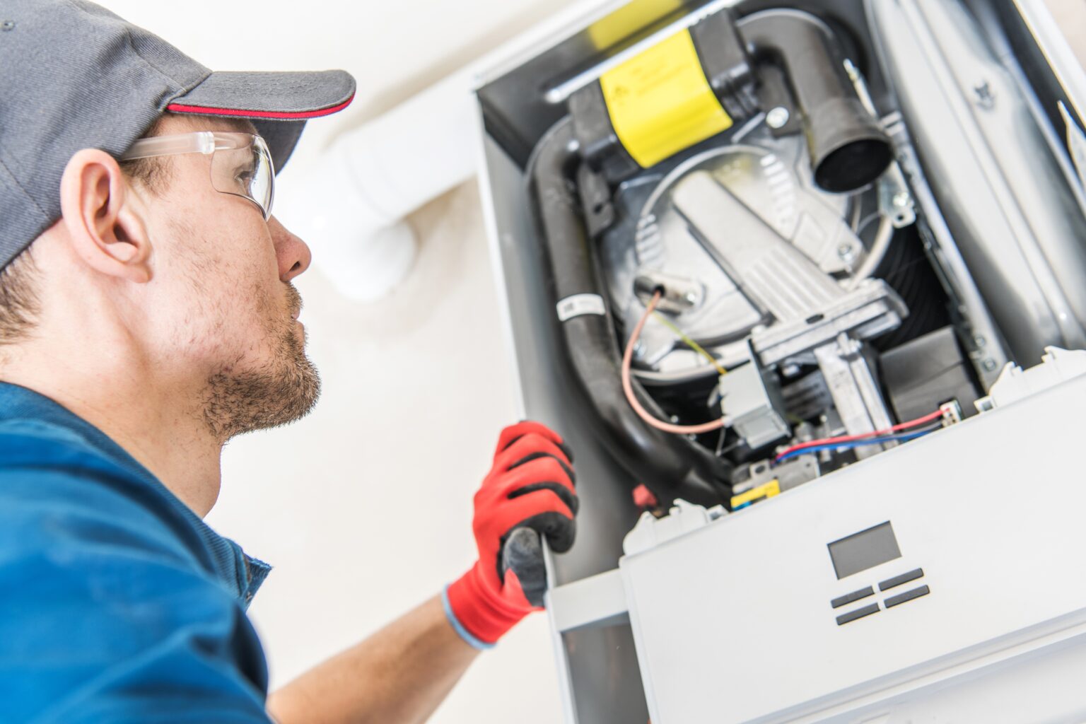 A technician in safety glasses and red gloves working inside an open gas furnace.