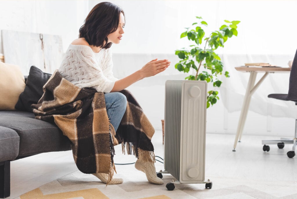 A woman wrapped in a blanket, warming her hands at home on a cold day.
