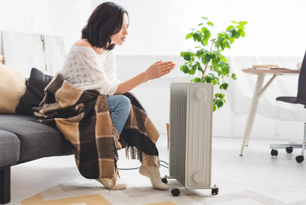 A woman wrapped in a blanket, warming her hands at home on a cold day.