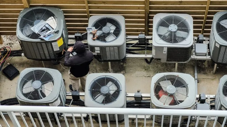 A row of commercial condenser fans on a building roof, with a technician alongside.