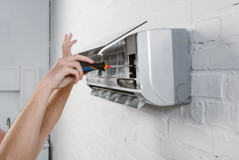 A technician opening the flap of a wall-mounted air conditioner to reach its filters.