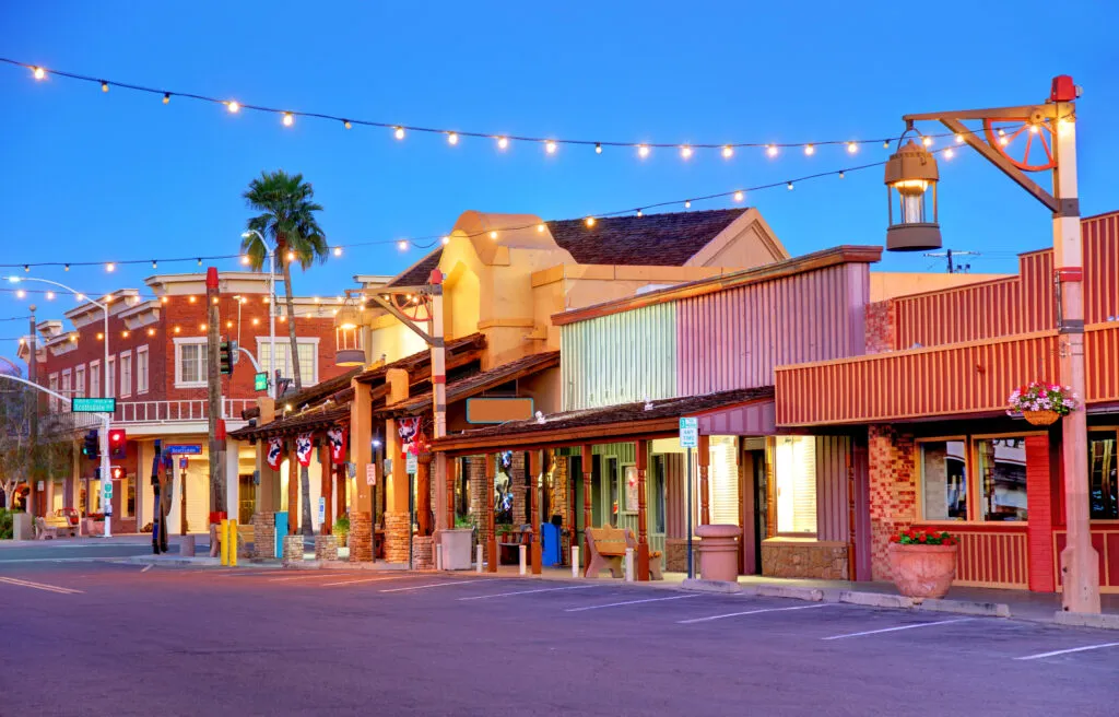 The western storefronts of Old Town Scottsdale lit up at dusk under strings of lights.