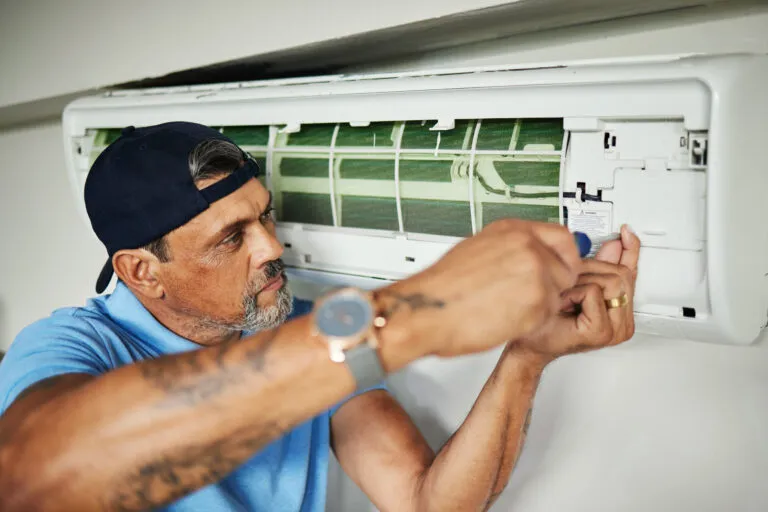 An air conditioning technician opening a wall-mounted indoor unit to service it.