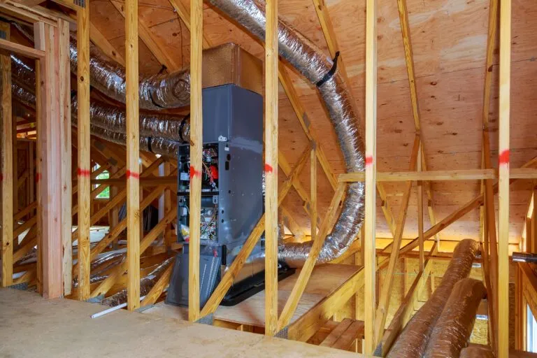 Ductwork and heating pipework being installed in a timber-framed building.