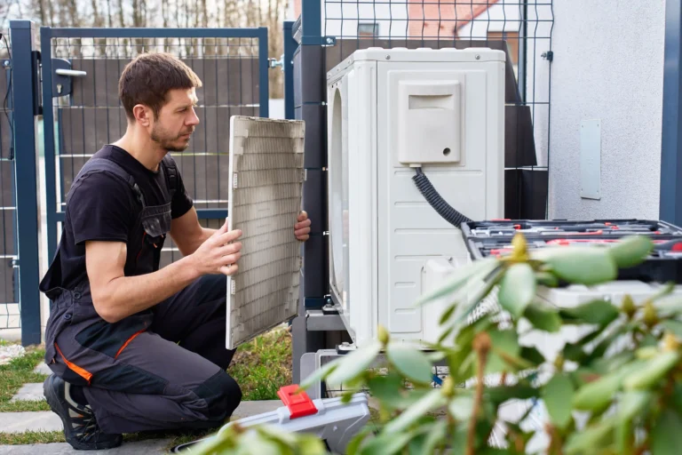 A technician holding a filter panel beside an outdoor air conditioning unit.